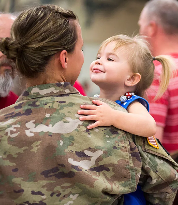 A person in a military uniform holds a small child.