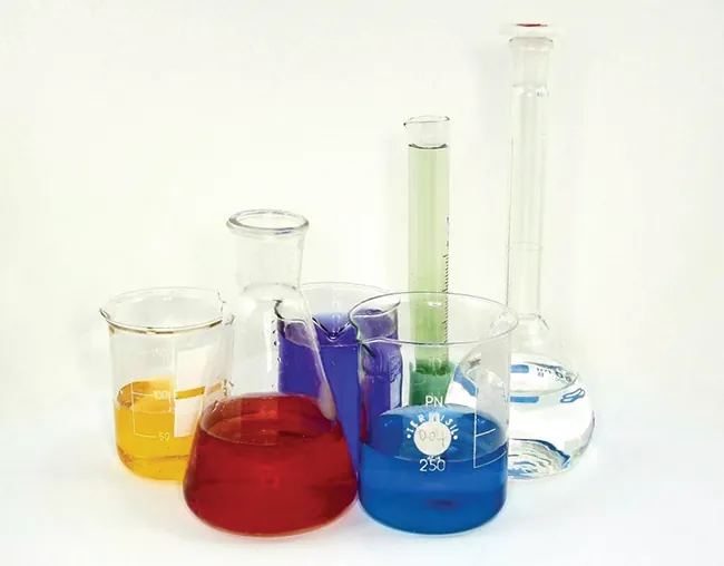 Se muestra una foto de vasos de precipitados, matraces y probetas graduadas. Cada pieza de cristalería contiene un líquido de diferente color.