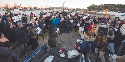 A group of people gathered outside, many with signs, listening to a person speaking.