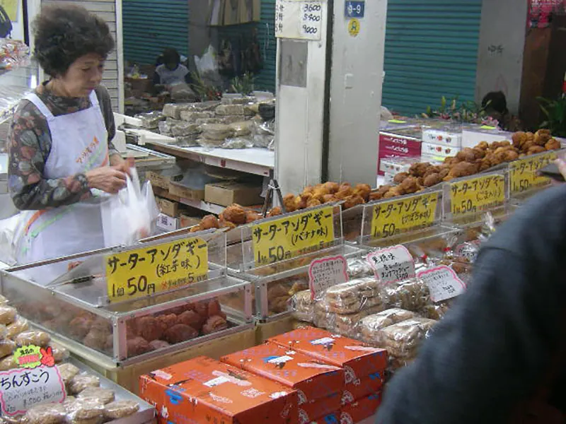 An older Japanese woman shopping at an outdoor market.