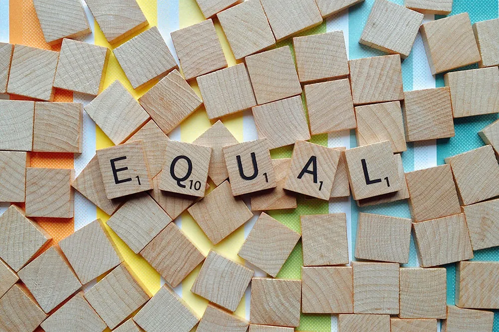 A photo shows Scrabble game tiles spelling out the word “equal.”