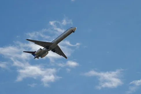 A photograph of an airplane flying in an upward direction is shown. The sky is partly cloudy.