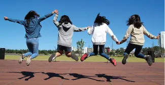 A photograph captures four people midair as they hold hands and jump.