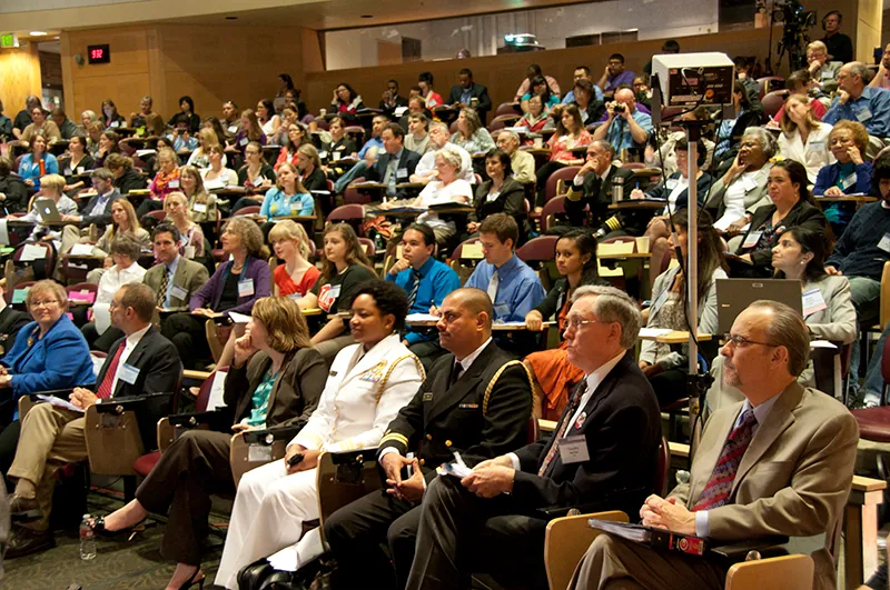 A diverse audience attends a town hall meeting in a auditorium.