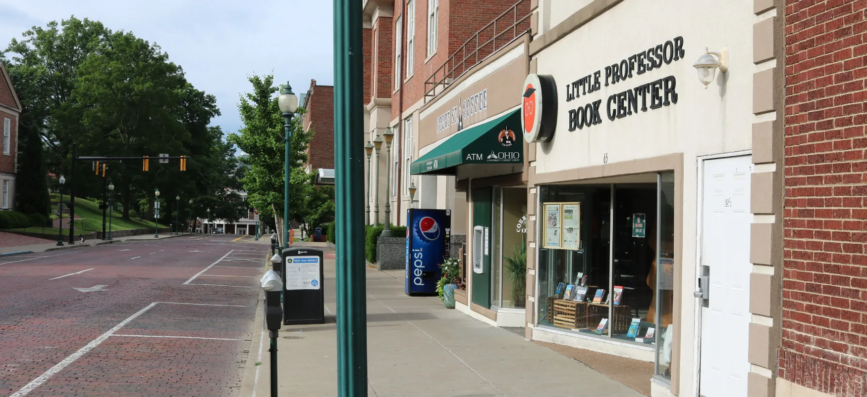 The Little Professor Book Center and another store are visible on the right side of a street. There is a Pepsi machine as well. There are no cars on the street.