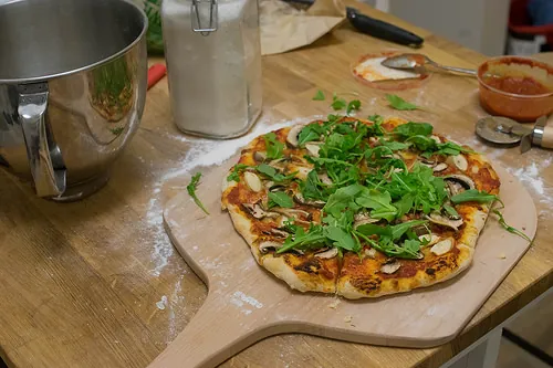 Image of a pizza peel with mushroom and arugula.