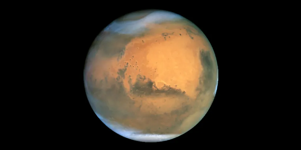 HST image of Mars. The hemisphere seen in this image shows dark regions on the lower half, a large reddish zone near the center, a polar cap and some clouds at the bottom, and a large area of wispy clouds near the top.