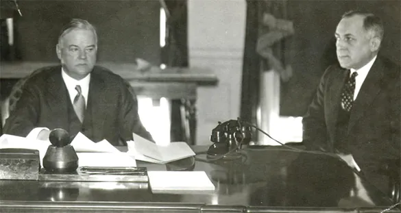 A photograph shows Herbert Hoover seated on the left at a desk with aide Theodore Joselin. The desk contains papers and a telephone. Hoover’s facial expression is grim and distracted.