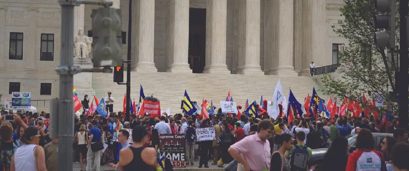 An image of a group of people standing in front of a building. Some people are holding signs.