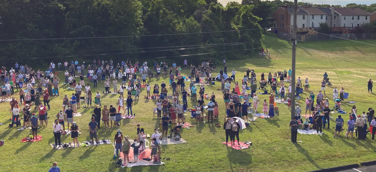 Photo of individuals and small groups of people gathered outdoors, socially distanced and wearing masks.