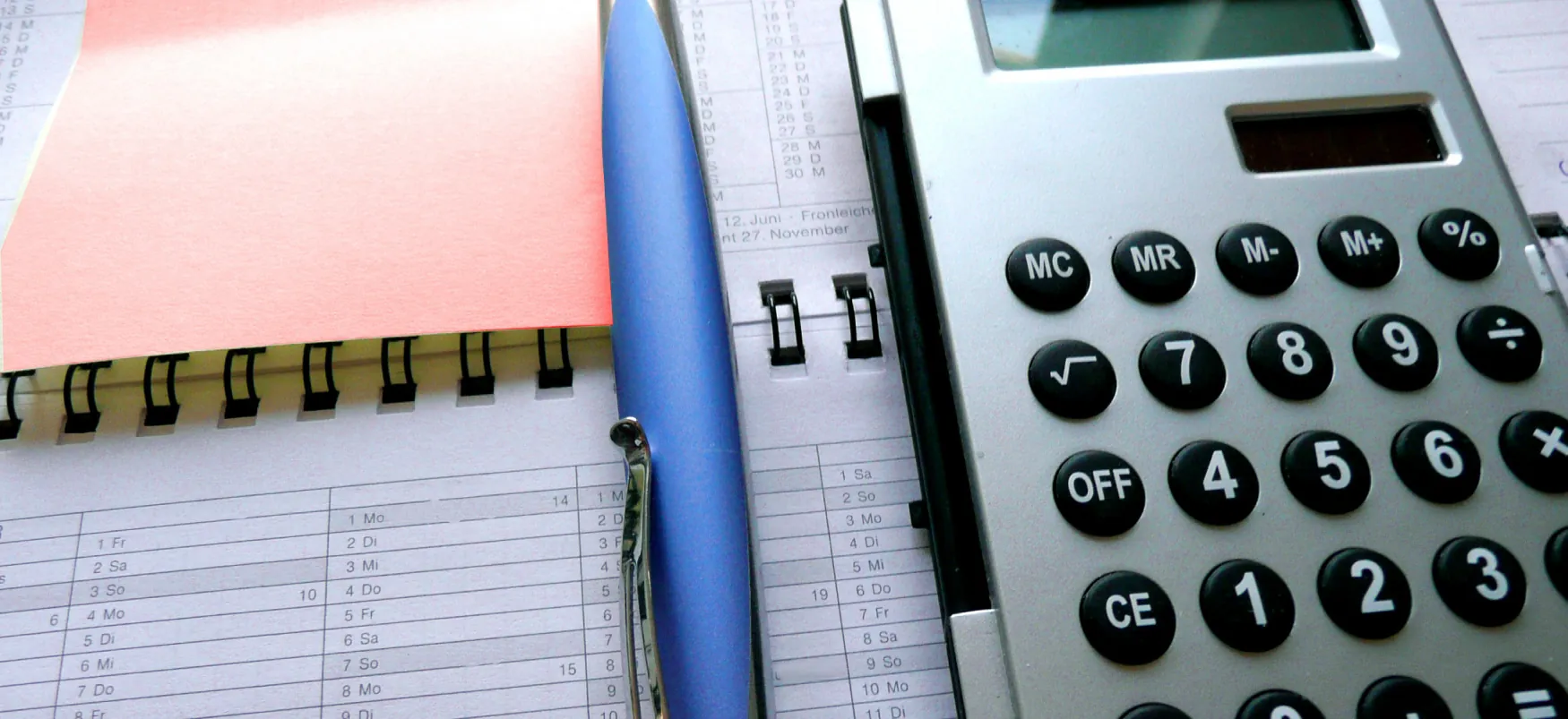 A pen and calculator are on top of a notebook showing financial figures and a sticky note.