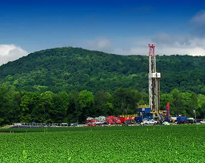  This is a photo of a shale drilling platform below a forested hill.