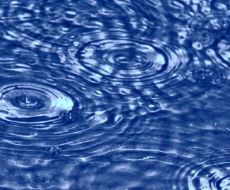 Se muestra una fotografía de ondas en el agua. Las ondas muestran un patrón de interferencia entre ellas.