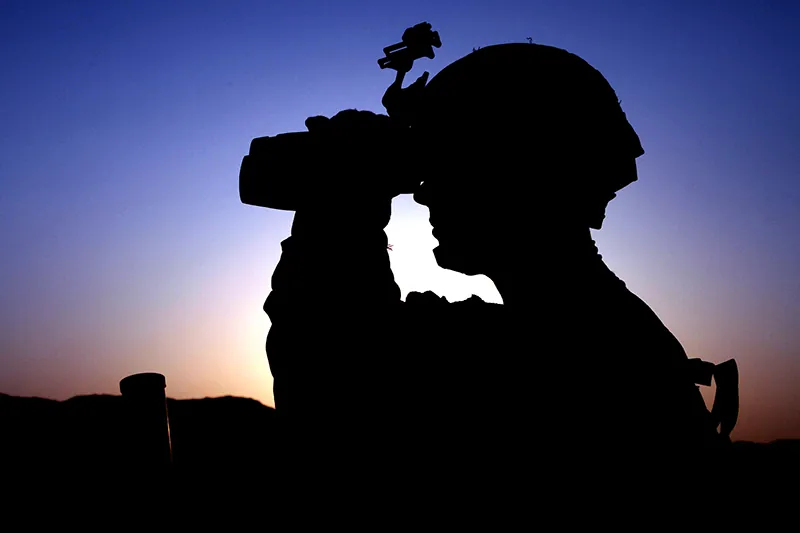 A soldier scans the ridge through binoculars.