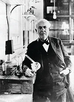 A photograph shows Thomas Edison in a brightly lit workroom. Beside him is a table holding an incandescent light bulb.