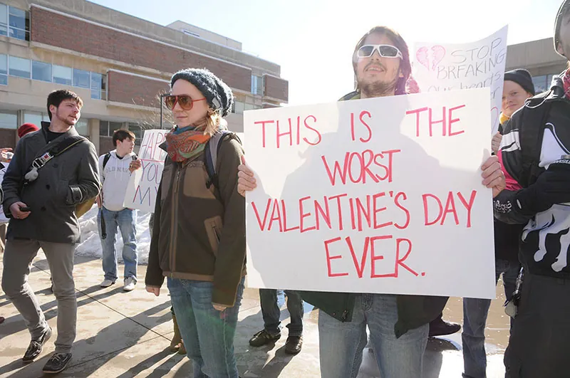 A group of protesters stands together. One holds a sign that reads, “This is the worst Valentine's Day Ever.”