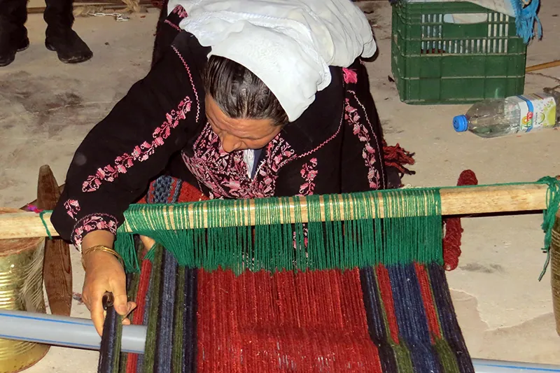 A woman with a head scarf sitting behind a simple wooden machine weaving wool.