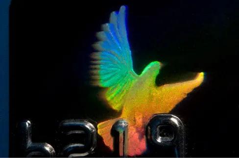 Fotografía de un holograma en una tarjeta de crédito. Tiene forma de pájaro y refleja muchos colores.