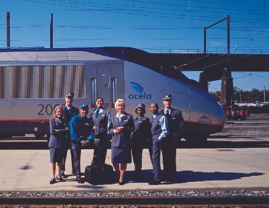 A photo of Amtrak staff standing on a train platform as a train passes behind them.