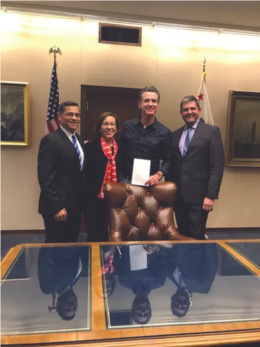 Four people stand behind a desk: (Left to Right) Attorney General Becerra, AARP Advocacy Manager Blanca Castro, Governor Newsom, and Assemblymember Jim Wood. Newsom holds a document.