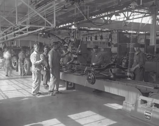 An image of a few people standing in an automotive plant next to some machinery.