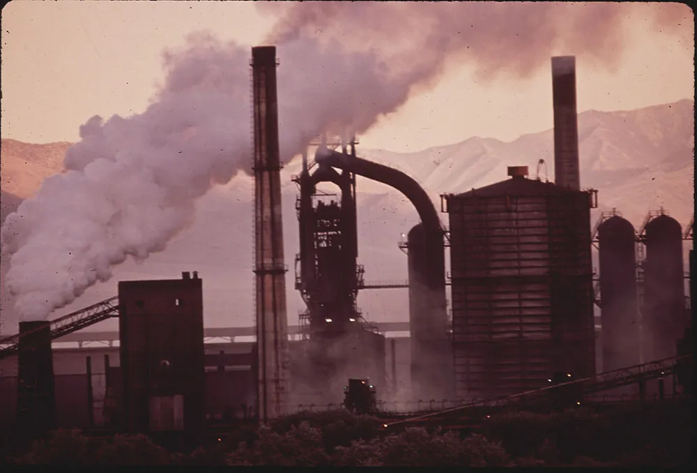 A photograph of an old steel mill at sunrise with smoke rising out of a smoke stack.
