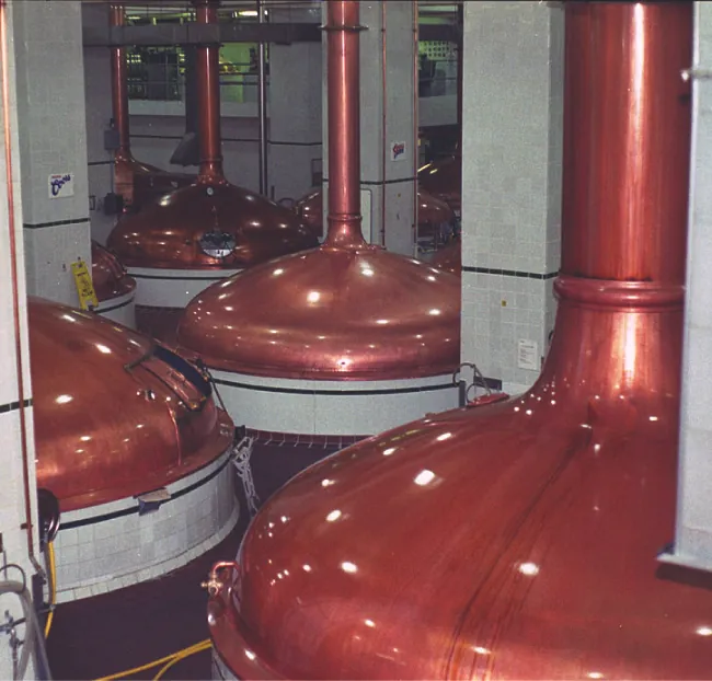 Se muestra una imagen de cuatro contenedores industriales de color cobre con una gran tubería conectada a la parte superior de cada uno.