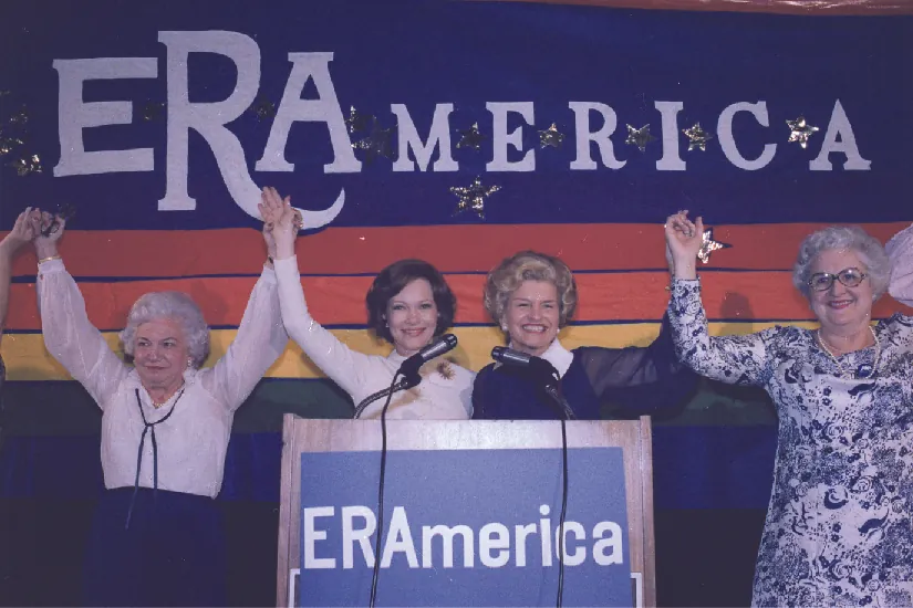 A photo of Rosalynn Carter and Betty Ford speaking at a rally in favor of the Equal Rights Amendment. Signs on stage read “ERAmerica.”