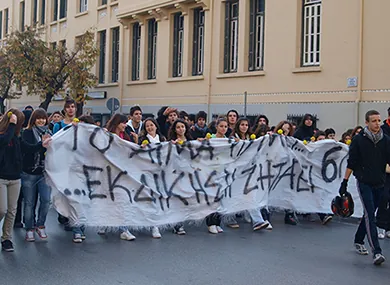 This is a photo of young people marching through a street holding a sign with Greek writing on it.