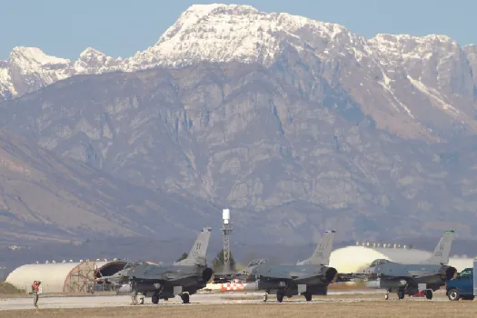 An image of several grounded fighter jets, with a mountain range in the background.
