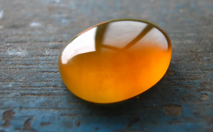 A photograph of a piece of gold-colored amber from Malaysia that has been rubbed and polished to a smooth, rounded shape.