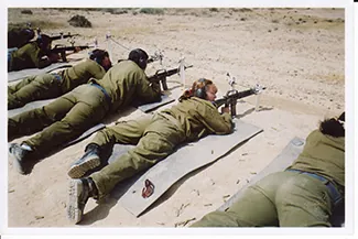 Zdjęcie przedstawia uzbrojoną żołnierkę pomiędzy grupą żołnierzy.