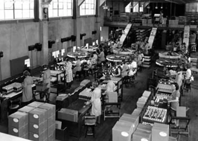 A photograph shows a warehouse full of people working with machines along assembly lines.