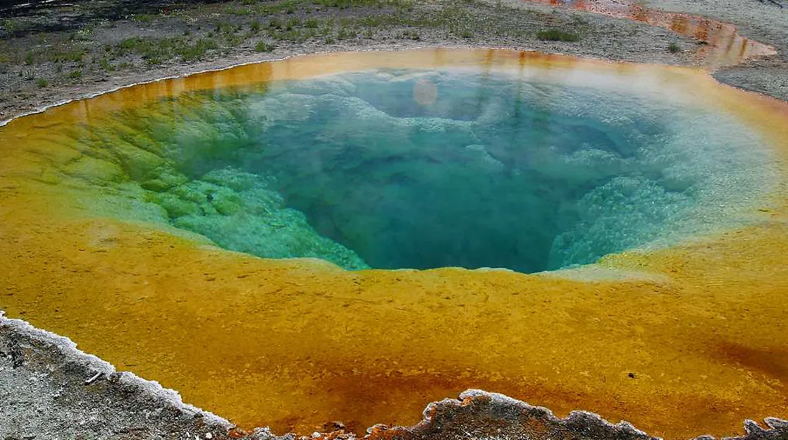 The photo shows a hot spring with a vivid blue color in the middle and a golden color around the edge.