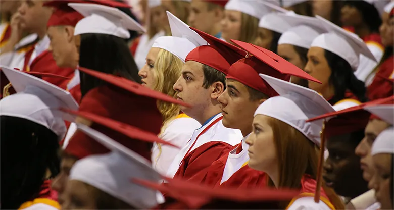 Zdjęcie przedstawia uczniów ubranych w charakterystyczne togi i birety podczas ceremonii ukończenia szkoły średniej.