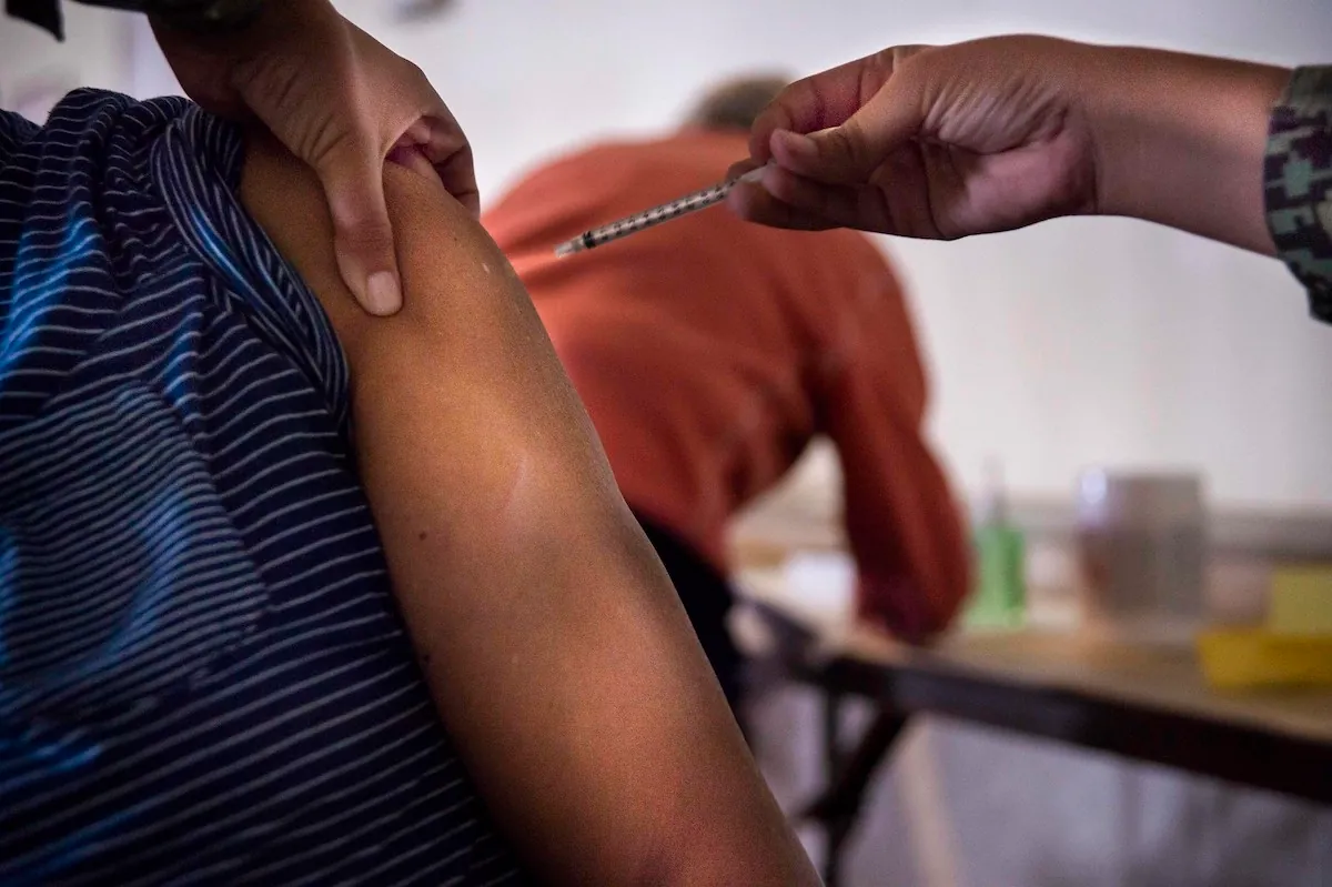 The photo shows a person receiving an injection in the arm.