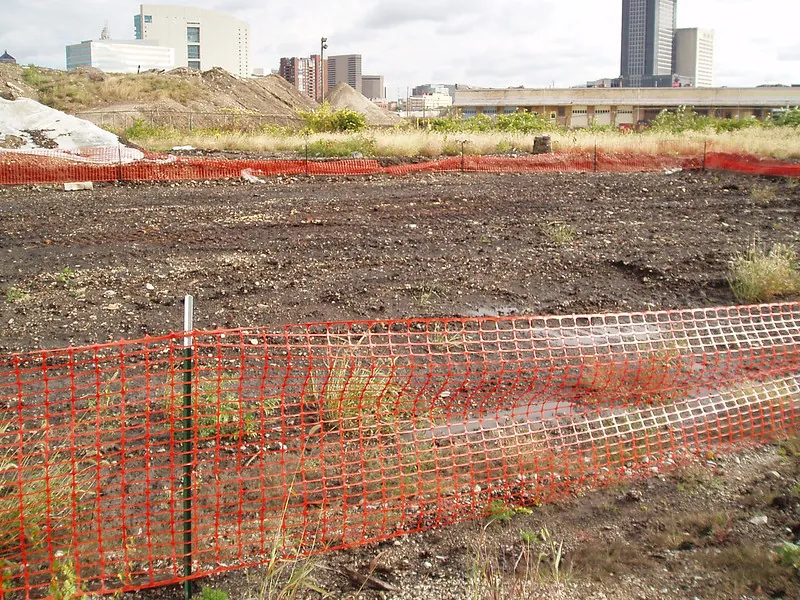 Cleared land with buildings visible in the background will be developed into a parking lot.