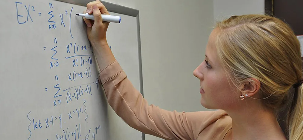 A woman is solving an equation on a white board.