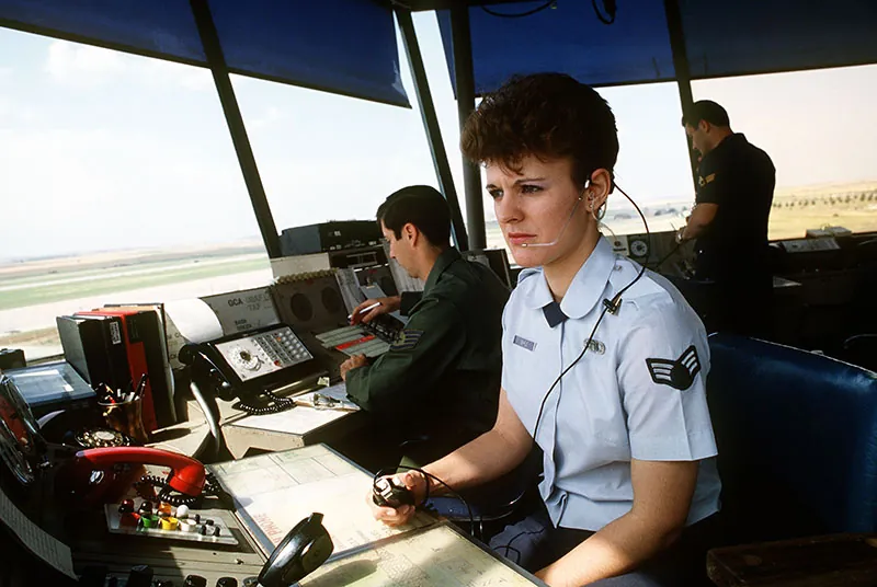 A photo shows air traffic controllers of the Air Force Communications Command working in the base control tower while observing incoming and outgoing aircraft.