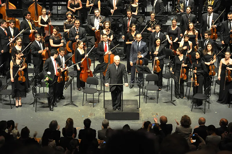 Orchestra members standing to acknowledge applause at the end of a performance.