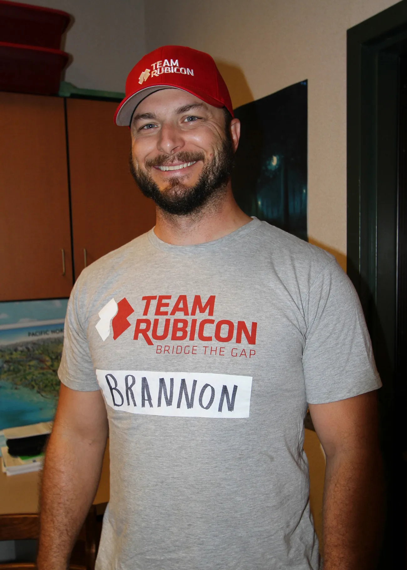 Photograph shows a man wearing a Team Rubicon hat, and Team Rubicon shirt.