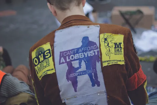 An image of the back a person wearing a jacket. A patch on the jacket reads “I can’t afford a lobbyist”.
