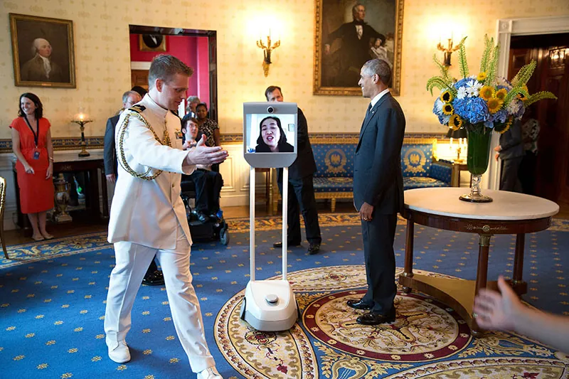Alice Wong participates via robot with then President Barack Obama in the 25th anniversary of the Americans with Disabilities Act. A soldier escorts the robot.