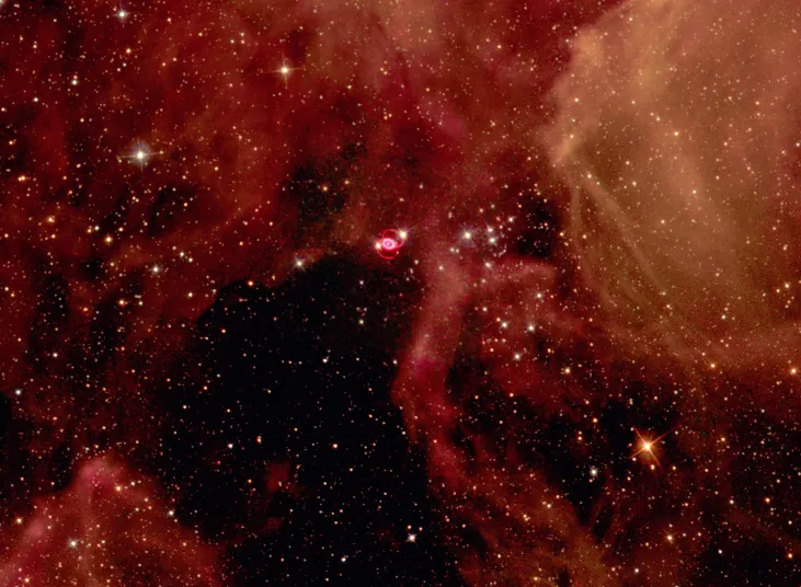Hubble Space Telescope image of SN 1987A. Large clouds of reddish gas and numerous background stars are seen in this wide-field image of SN 1987A. The supernova remnant is the small, bright red oval near center, connected to two fainter red arcs of light above and below the bright oval.