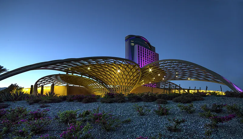 A large, modern building in a desert with several wing-like structures in the shape of nets surrounding it.