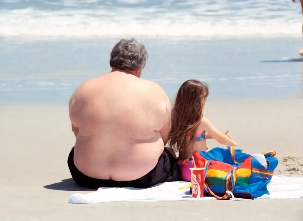 A large man is shown here sitting on a beach with a young girl.