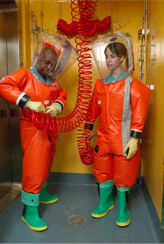 A photo of two lab workers in suits that completely covers them (including their faces and hands).