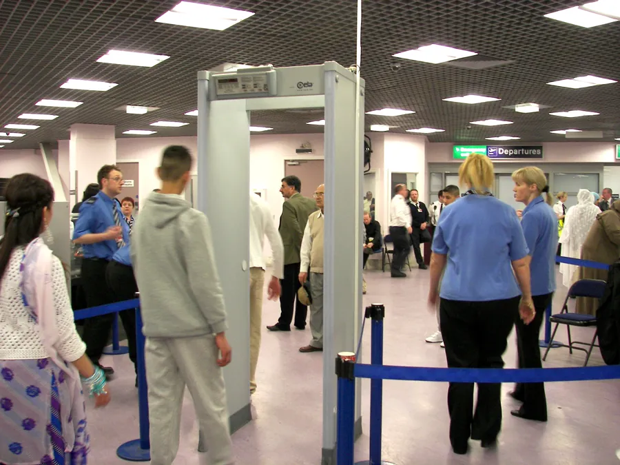 Photograph of people around a security gate at an airport departure terminal.