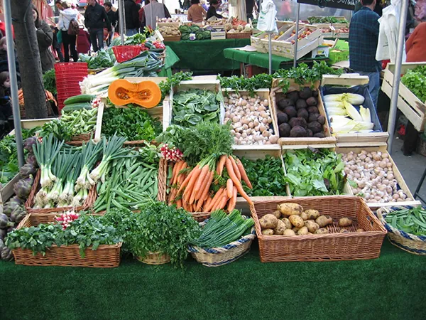 A French open air market sells a variety of fresh produce in wooden crates and baskets, including carrots, potatoes, and green onions among others.