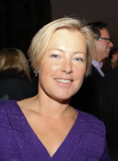 A headshot of a woman with short blond hair. Several other people are visible in the background.